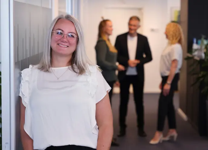 Leende affärskvinna på jobbet med kollegor som pratar i bakgrunden på kontoret.